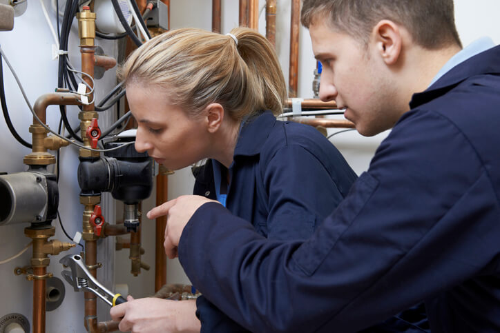 Female Trainee Plumber Working On Central Heating Boiler